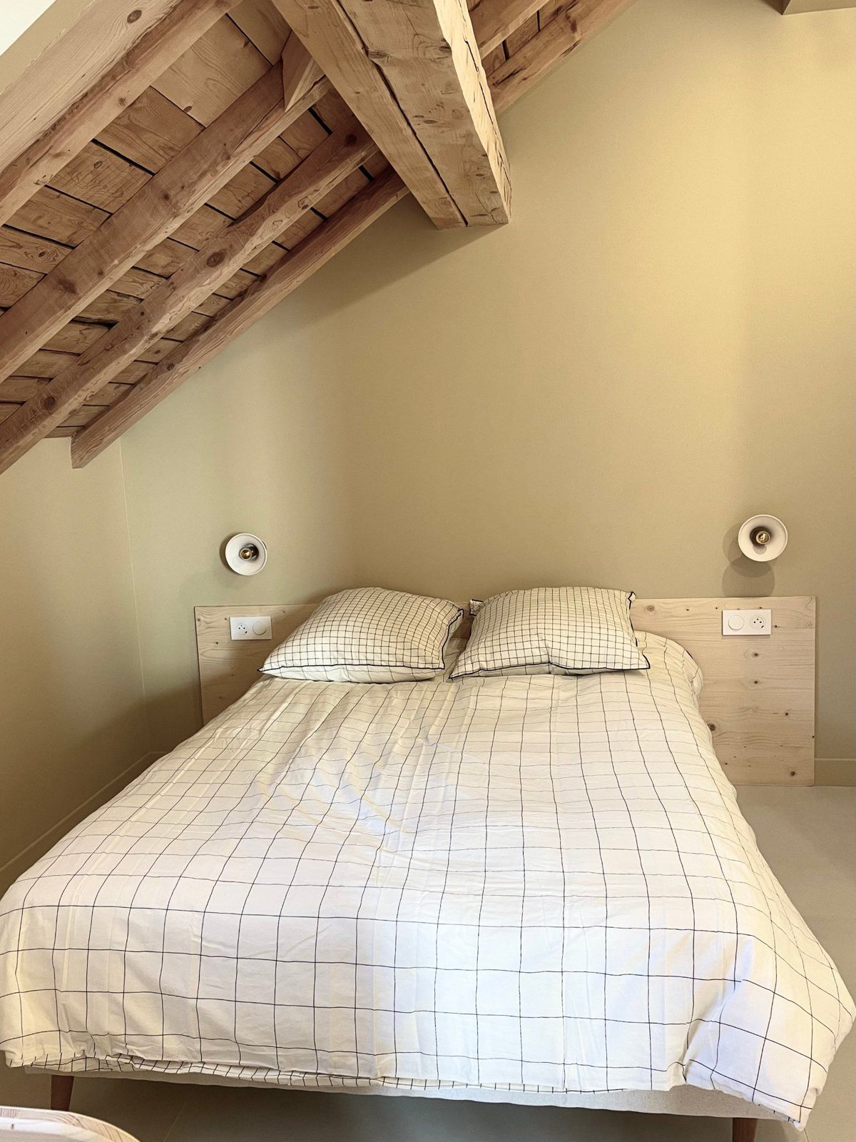 Lit double sous la charpente en bois, appliques de part et d'autre