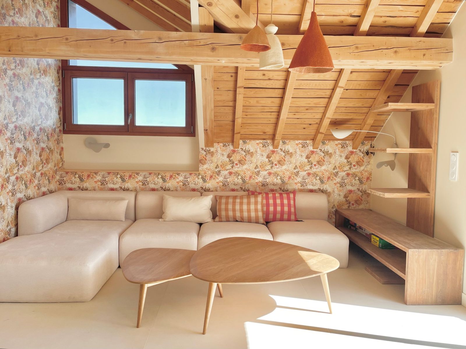 Le coin salon sous la charpente : grand canapé, tables basses en bois et papier peint fleuri