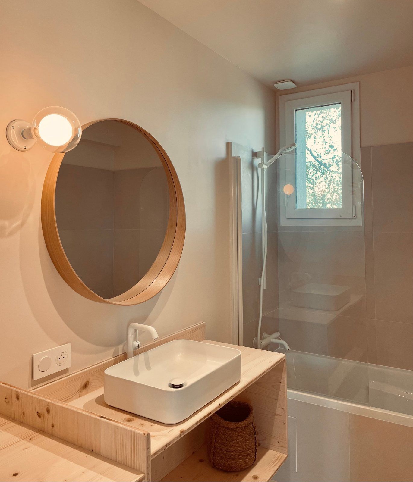 La salle de bain avec baignoire, vasque sur meuble en bois et miroir rond
