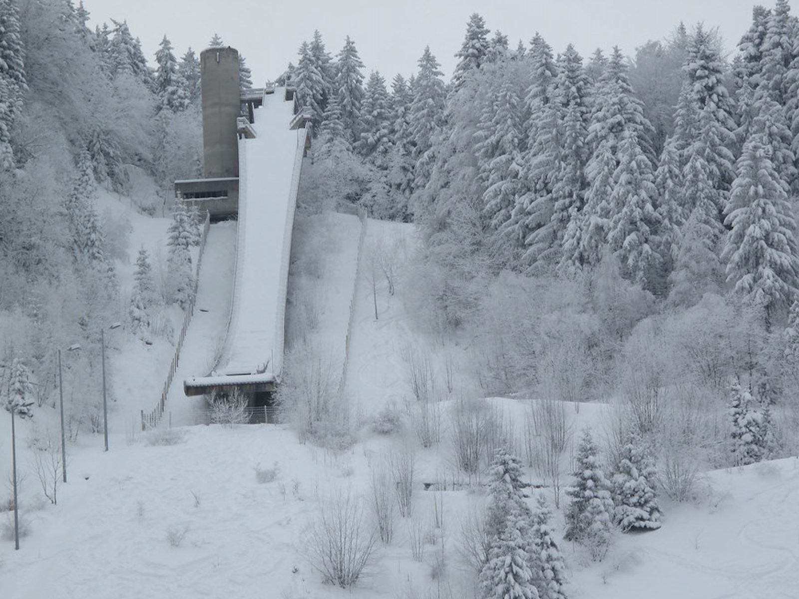 Le tremplin olympique de Saint-Nizier aujourd'hui, sa tour de béton et sa piste sous la neige, entourés de sapins blancs